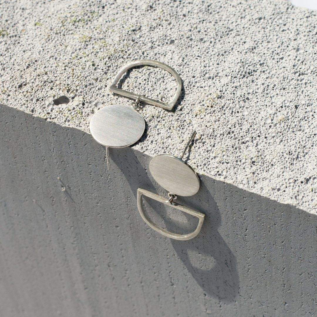 Minimalist silver geometric earrings on textured concrete surface showcasing Australian fashion brands' sustainable jewelry designs.