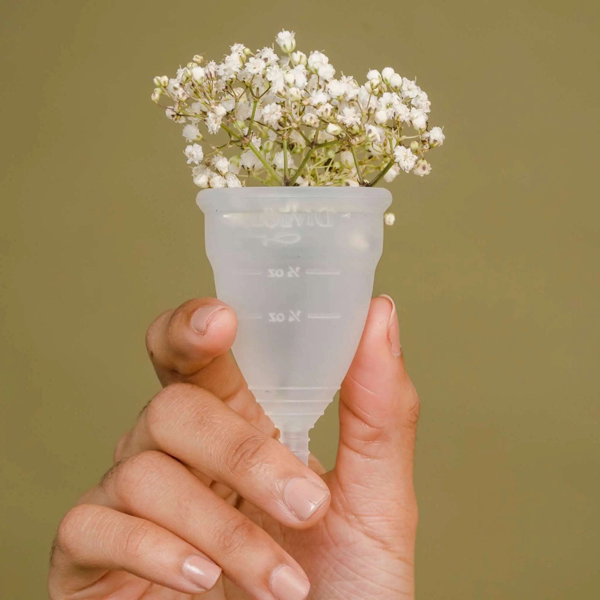 Hand holding a transparent menstrual cup with small white flowers inside, symbolizing eco-friendly birth-control and period products.