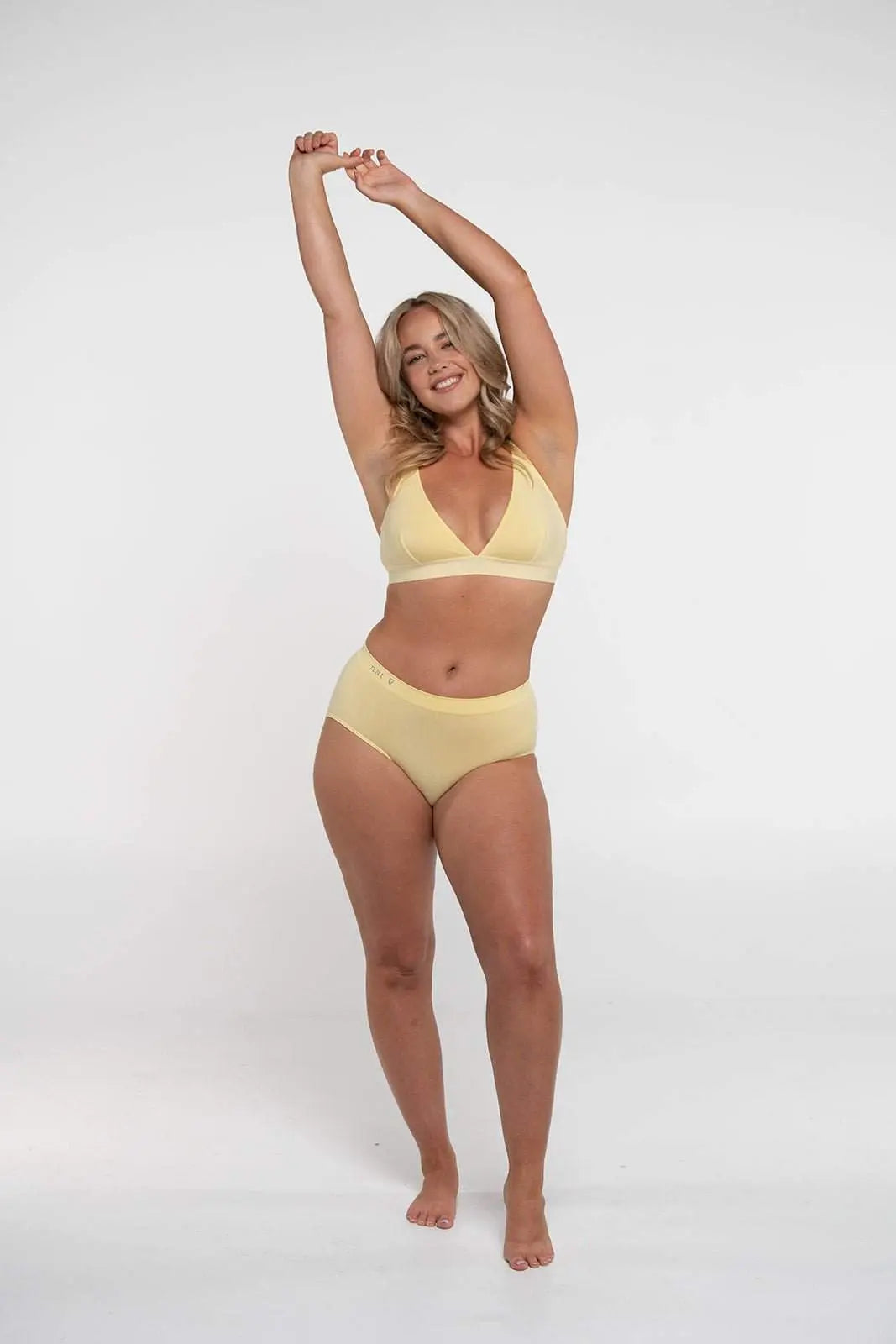 Smiling woman wearing yellow Lenzing Modal underwear set standing with arms raised against white background