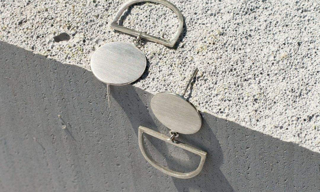 Minimalist silver geometric earrings on textured concrete surface showcasing Australian fashion brands' sustainable jewelry designs.