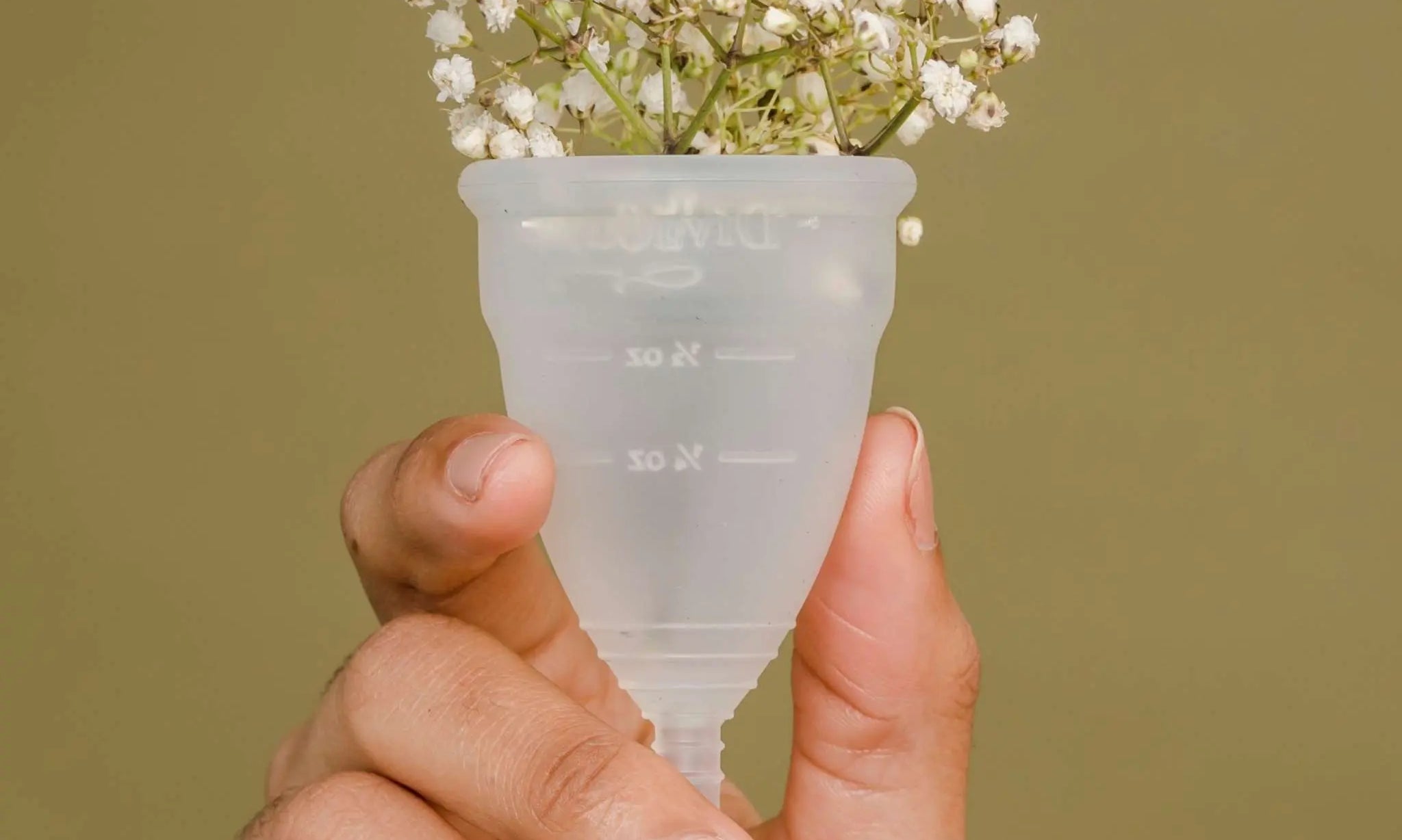 Hand holding a transparent menstrual cup with small white flowers inside, symbolizing eco-friendly birth-control and period products.