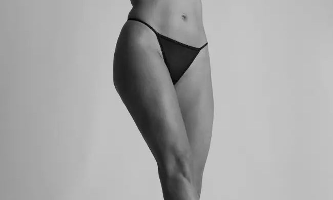 Woman wearing a black G-string, black bra, and cowboy boots with a hat in a studio setting