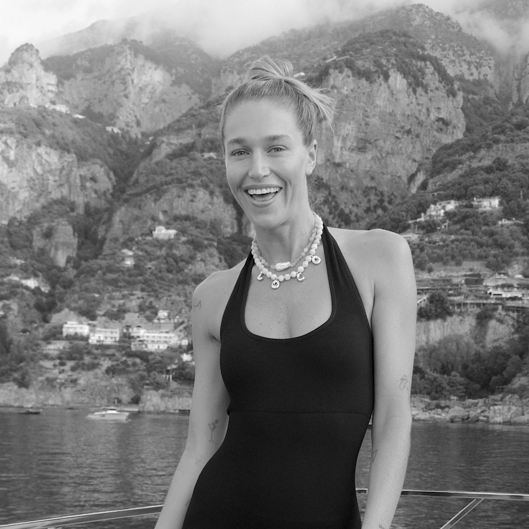 Woman in a black swimsuit standing on a boat with a mountainous landscape in the background